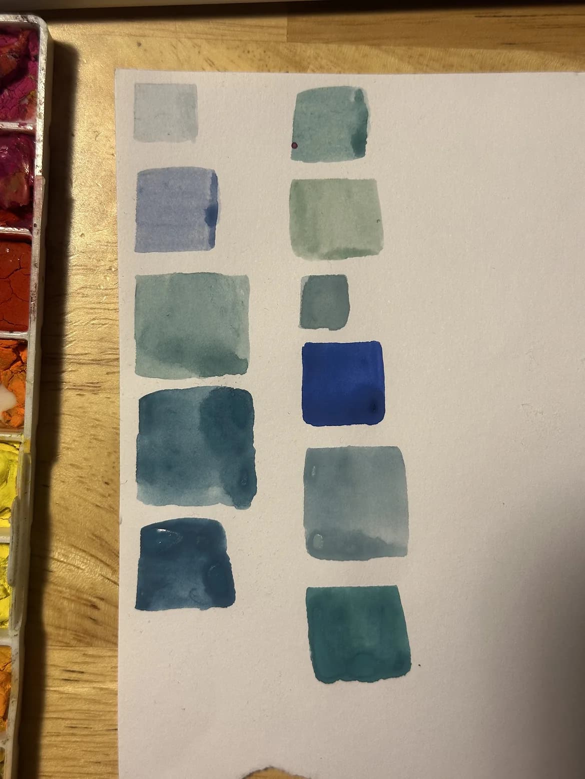 Hand-painted watercolor swatches in blues and teals on white paper beside a paint palette